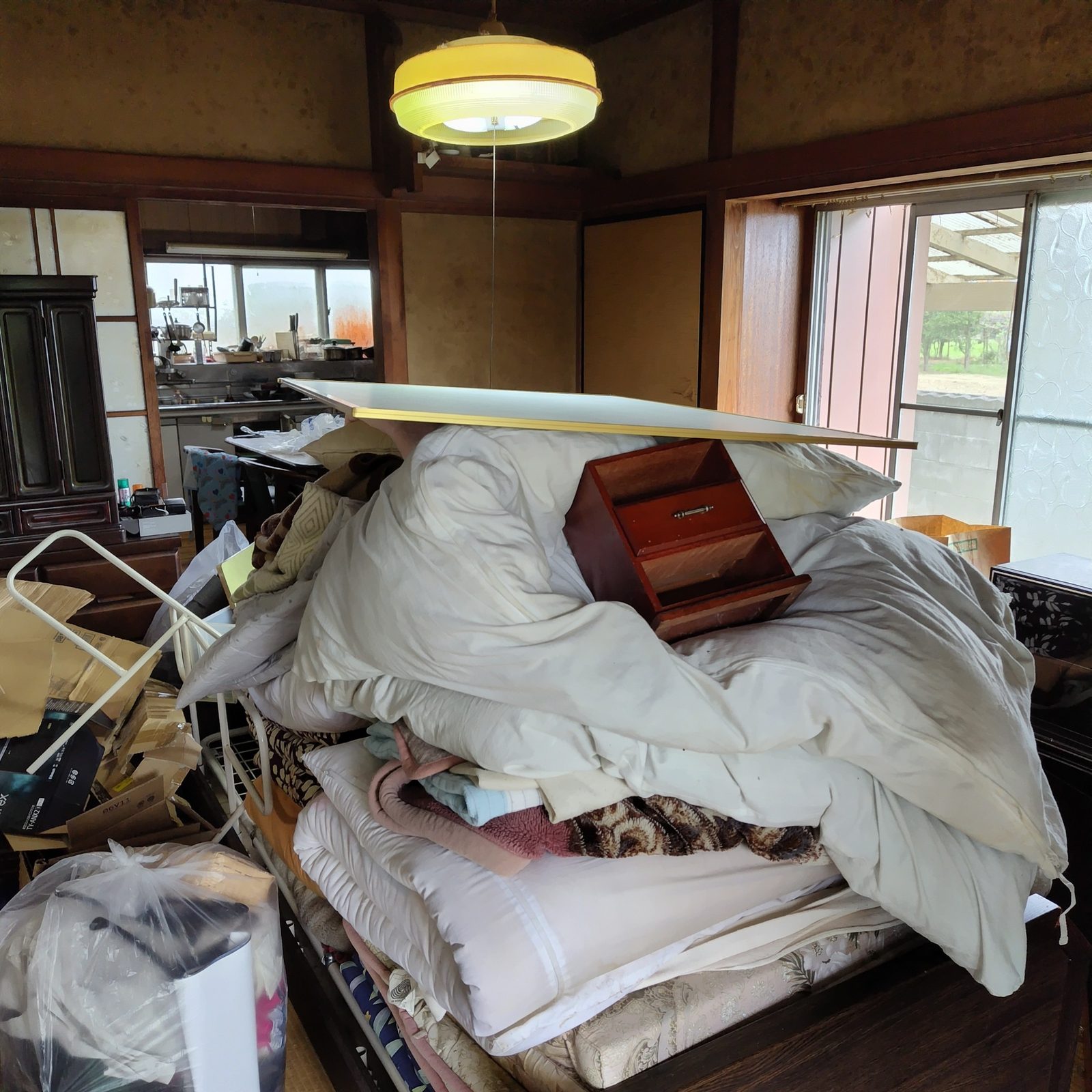 布団や家具が積まれた片付け前の部屋